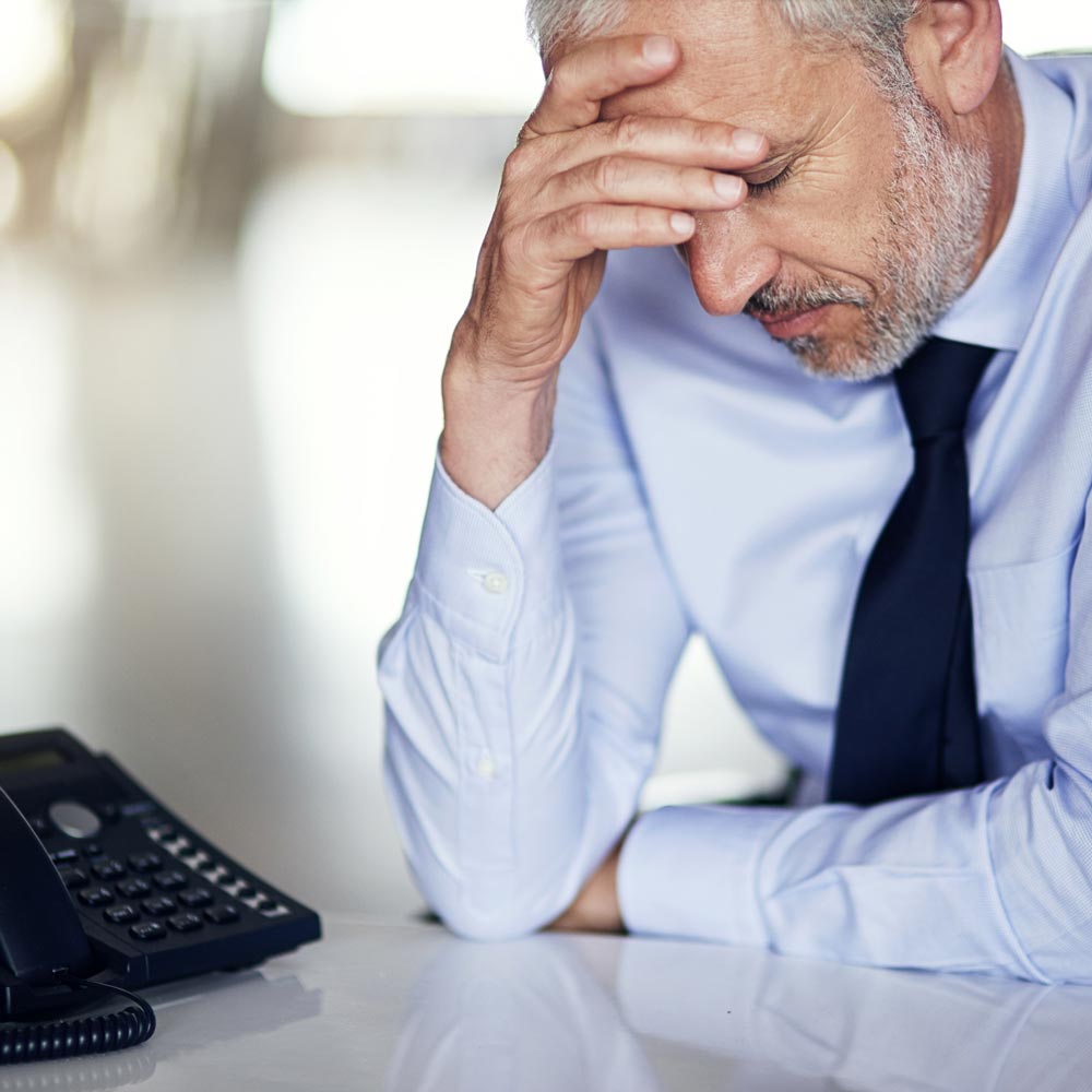 gestresster Mann am Arbeitsplatz mit Verspannungen und Schmerzen